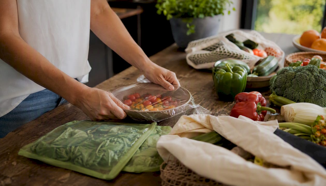 Hands sealing food with plastic-free cling wrap in kitchen