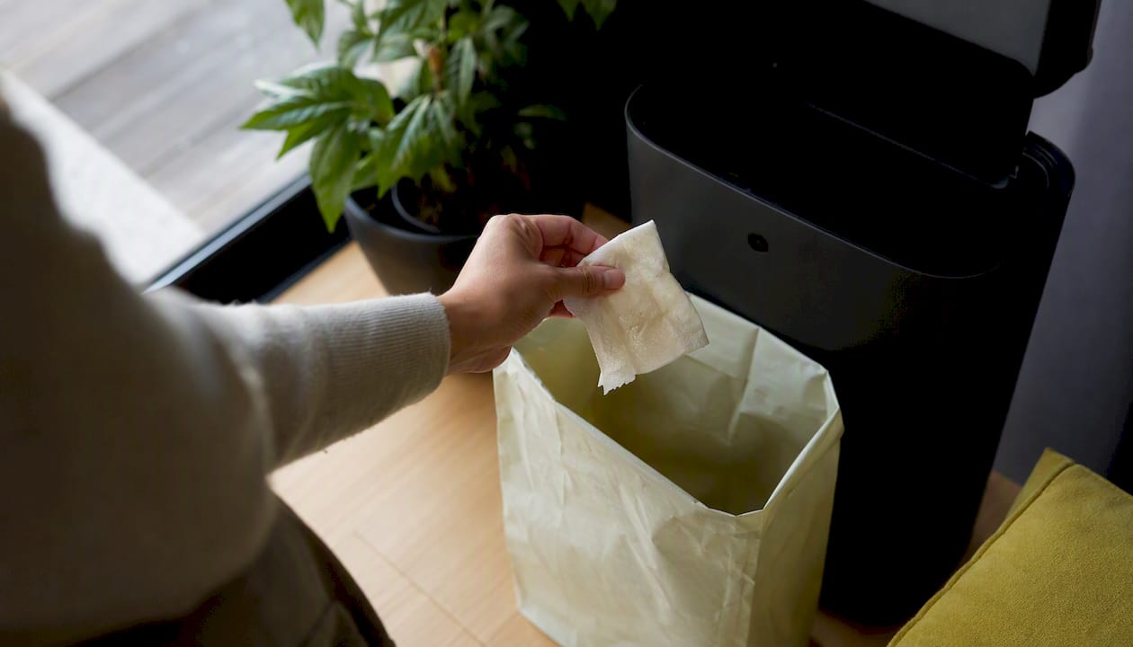 Hand disposing wipe into bin near toilet