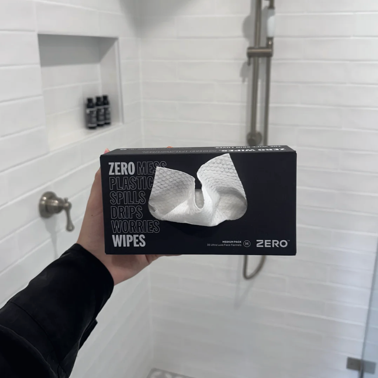 Person holding a box of 'Zero Men's Plastic Spills Drifts Worries Wipes' in a bathroom.