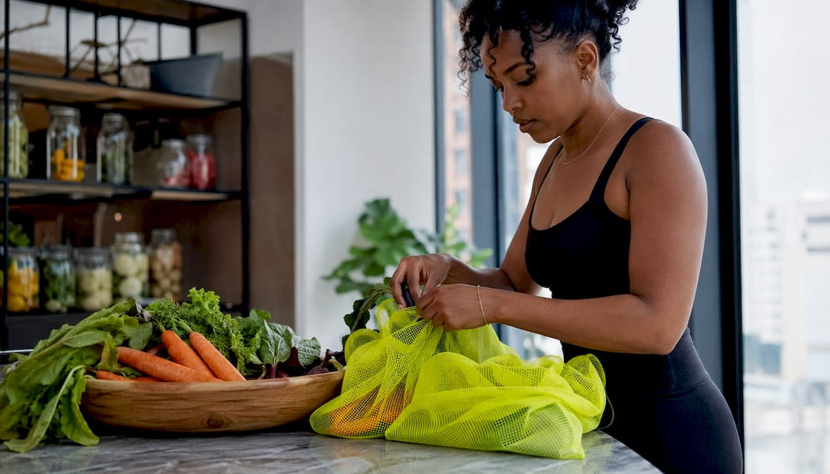 Woman placing vegetables in mesh bags on kitchen counter