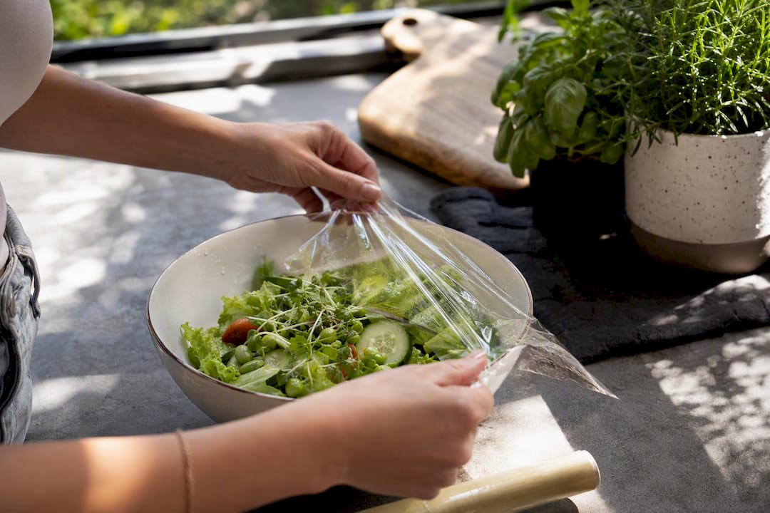 Hands wrapping salad bowl with eco-friendly cling wrap