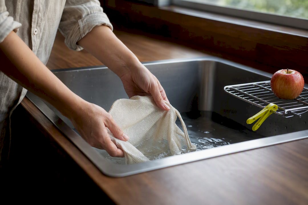 Hands gently rinsing reusable produce bag